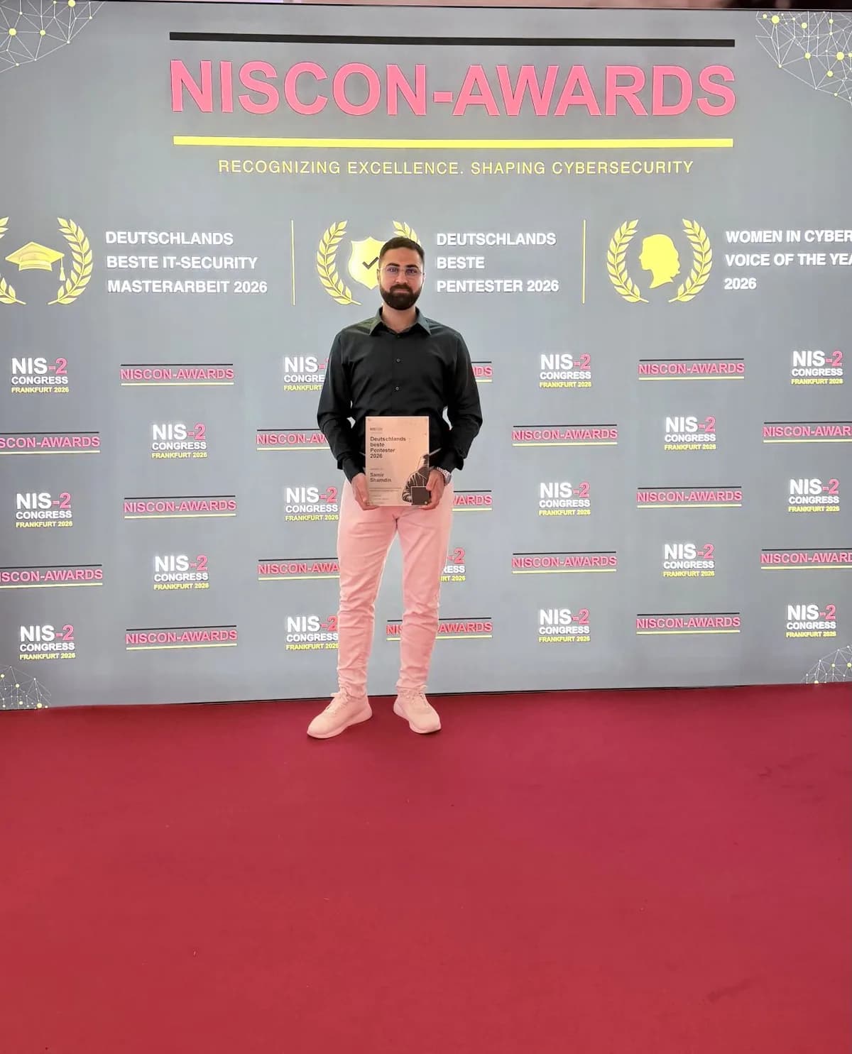 Samir Shamdin mit der Urkunde 'Deutschlands beste Pentester 2026' vor der NISCON-Awards-Wand auf dem NIS-2-Congress in Frankfurt